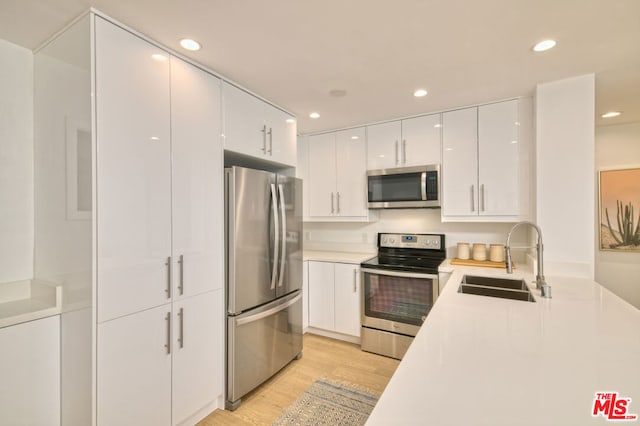 kitchen featuring appliances with stainless steel finishes, light hardwood / wood-style floors, white cabinets, and sink