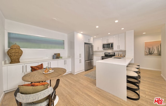 kitchen with white cabinets, appliances with stainless steel finishes, sink, kitchen peninsula, and light hardwood / wood-style flooring