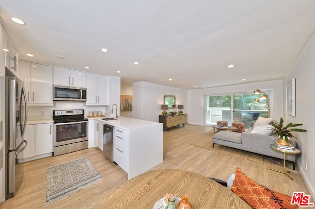 kitchen with kitchen peninsula, stainless steel appliances, light wood-type flooring, white cabinets, and sink