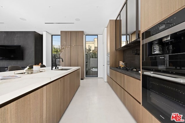 kitchen featuring floor to ceiling windows, sink, black double oven, and light stone countertops