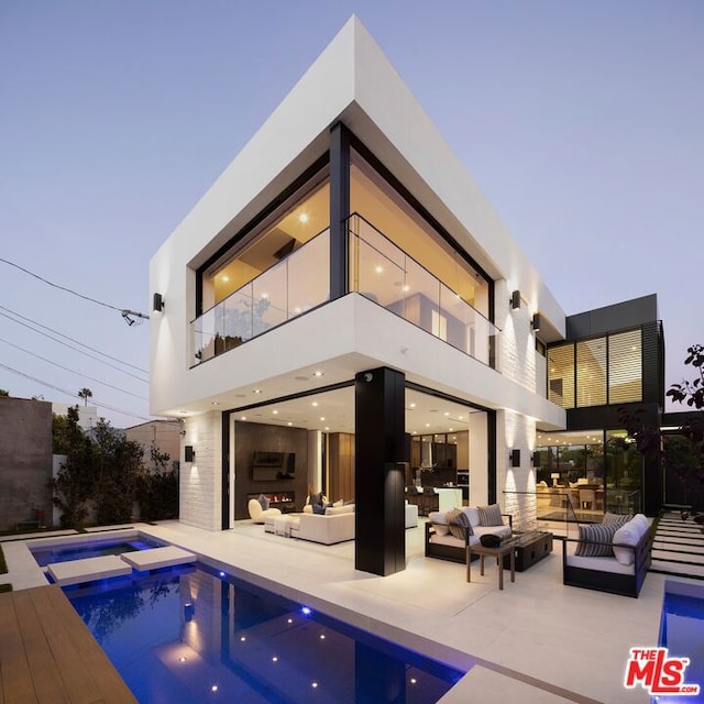 back house at dusk with an outdoor living space, a swimming pool with hot tub, a balcony, and a patio