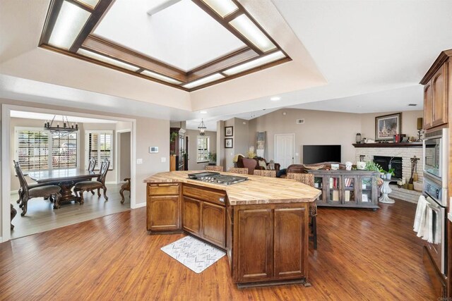 kitchen with a brick fireplace, a kitchen island, an inviting chandelier, a tray ceiling, and appliances with stainless steel finishes