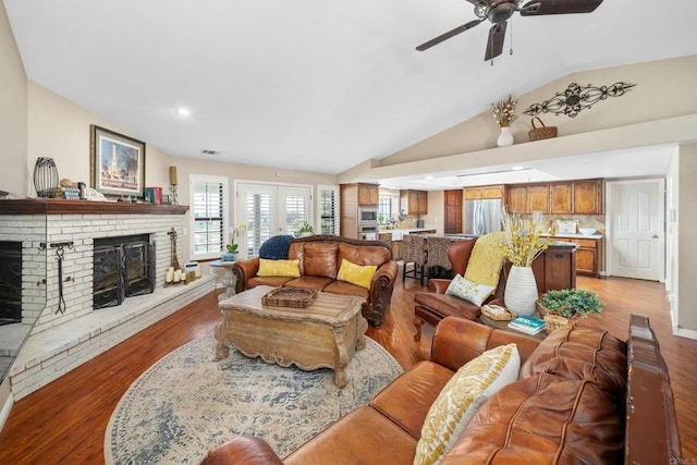 living room featuring light hardwood / wood-style floors, a brick fireplace, ceiling fan, and vaulted ceiling