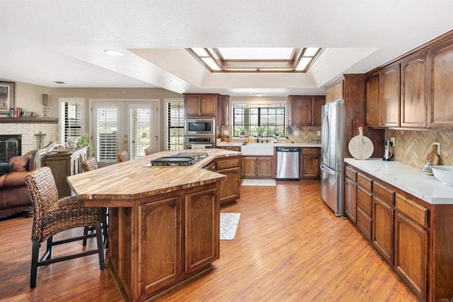 kitchen featuring a kitchen island, stainless steel appliances, backsplash, a brick fireplace, and a tray ceiling