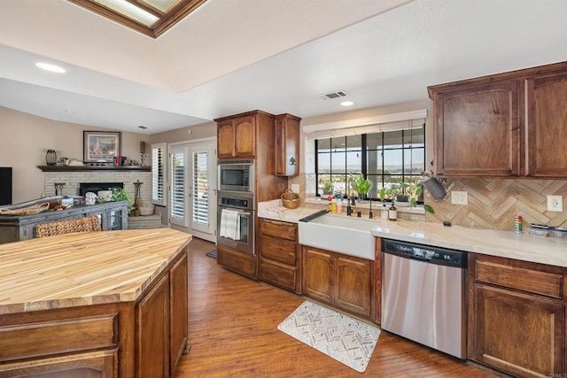 kitchen with dark wood-type flooring, stainless steel appliances, sink, backsplash, and a brick fireplace