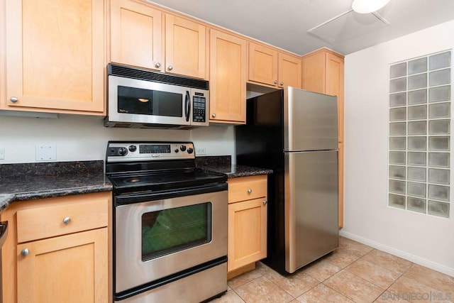 kitchen featuring appliances with stainless steel finishes, dark stone countertops, light brown cabinets, and light tile patterned floors