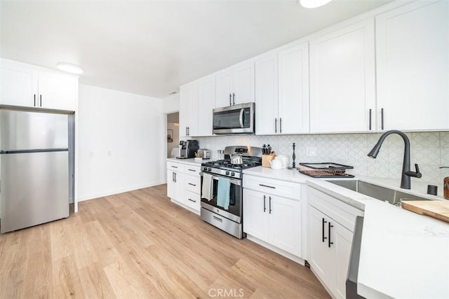 kitchen with sink, appliances with stainless steel finishes, backsplash, light hardwood / wood-style floors, and white cabinets