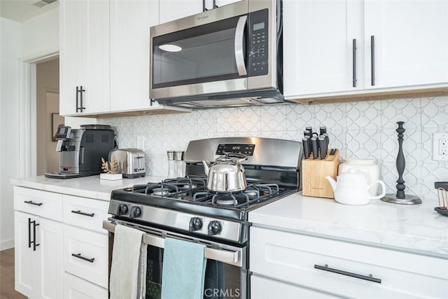 kitchen featuring decorative backsplash, white cabinets, and stainless steel appliances