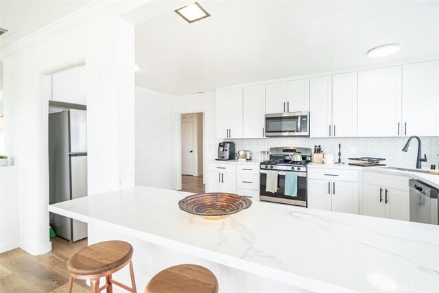 kitchen with tasteful backsplash, a kitchen bar, sink, white cabinetry, and stainless steel appliances