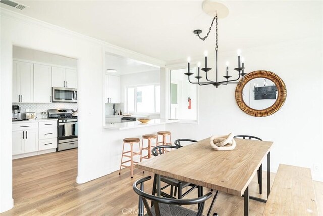 dining room featuring light hardwood / wood-style floors, crown molding, and a notable chandelier