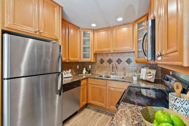 kitchen with stainless steel appliances, dark stone countertops, light hardwood / wood-style flooring, and sink