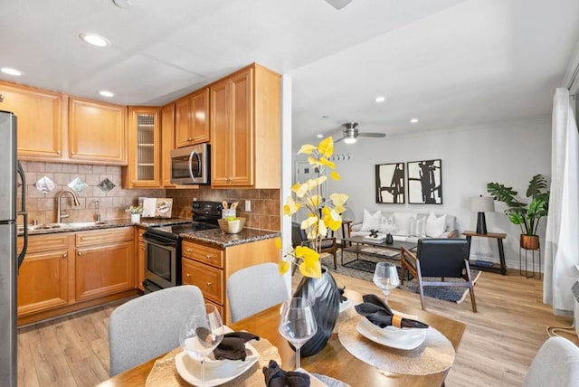 kitchen featuring ceiling fan, stainless steel appliances, light wood-type flooring, dark stone counters, and sink