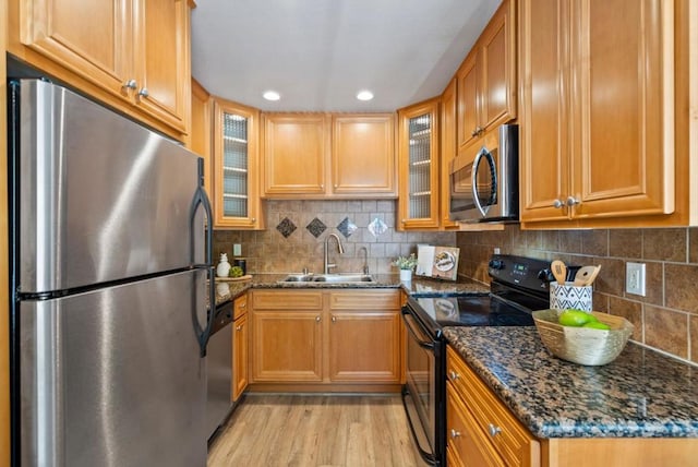 kitchen with light hardwood / wood-style floors, stainless steel appliances, backsplash, dark stone counters, and sink