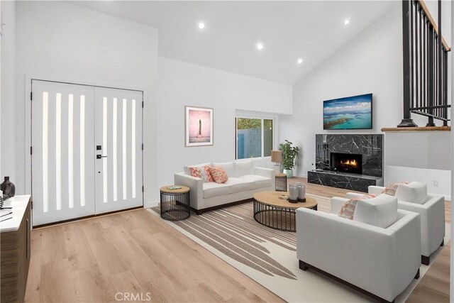 living room with high vaulted ceiling, light wood-type flooring, and a high end fireplace