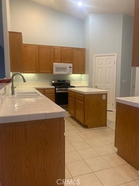 kitchen with tile countertops, a towering ceiling, sink, stainless steel range oven, and light tile patterned floors