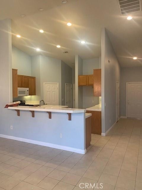 kitchen with light tile patterned floors, kitchen peninsula, high vaulted ceiling, a breakfast bar, and sink