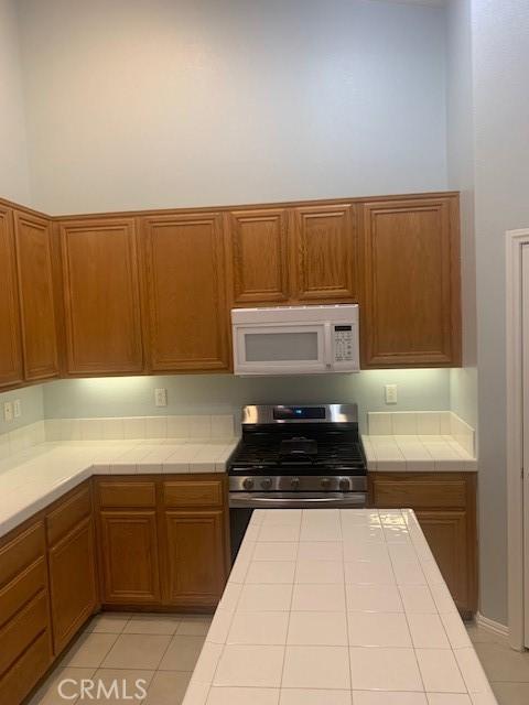 kitchen with light tile patterned flooring, tile countertops, and stainless steel range with gas cooktop