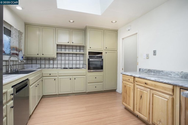 kitchen featuring a skylight, appliances with stainless steel finishes, decorative backsplash, light hardwood / wood-style flooring, and sink