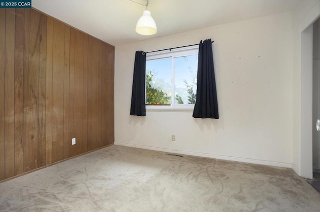 spare room featuring light colored carpet and wood walls