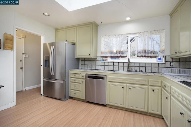 kitchen featuring tile countertops, stainless steel appliances, backsplash, light hardwood / wood-style flooring, and sink