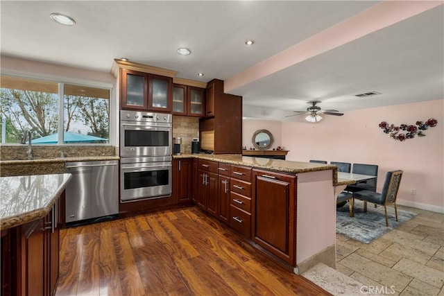 kitchen featuring appliances with stainless steel finishes, decorative backsplash, kitchen peninsula, and light stone countertops