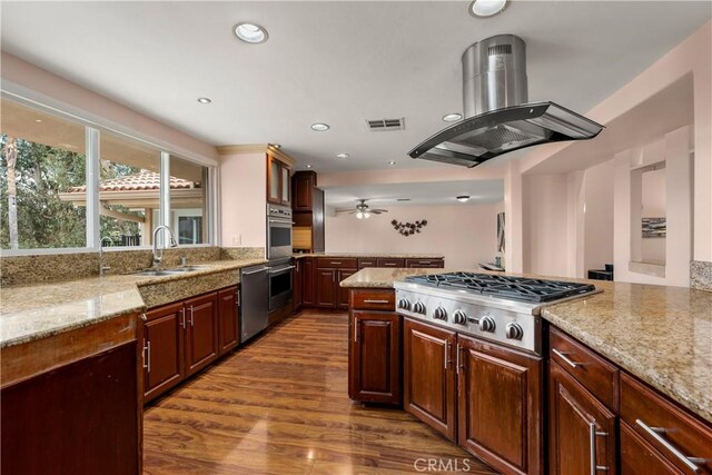 kitchen with ceiling fan, sink, island exhaust hood, appliances with stainless steel finishes, and light stone counters