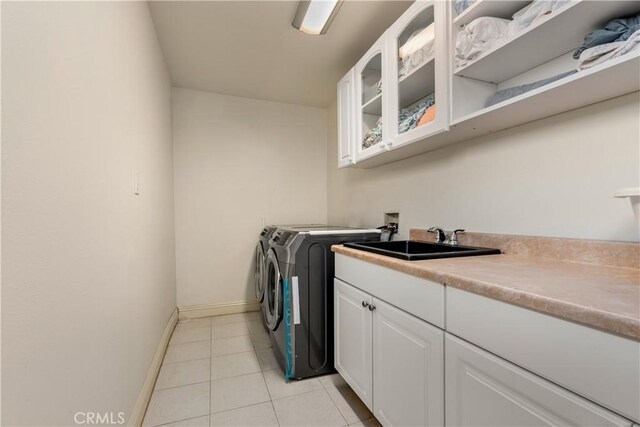 clothes washing area with cabinets, light tile patterned flooring, washing machine and clothes dryer, and sink