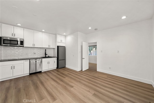 kitchen featuring backsplash, sink, white cabinetry, light wood-type flooring, and appliances with stainless steel finishes