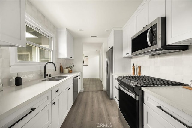 kitchen featuring white cabinetry, appliances with stainless steel finishes, tasteful backsplash, wood-type flooring, and sink