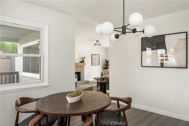 dining area featuring a brick fireplace, dark hardwood / wood-style flooring, and a notable chandelier