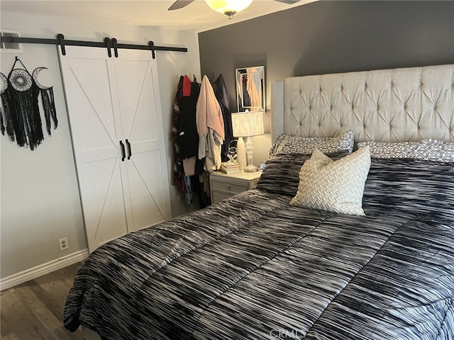 bedroom featuring a barn door, ceiling fan, and dark hardwood / wood-style floors