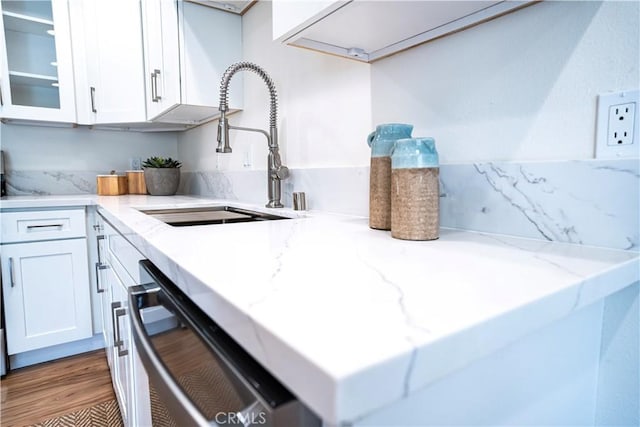 kitchen featuring dishwasher, sink, white cabinetry, light wood-type flooring, and light stone countertops