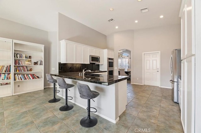 kitchen with arched walkways, stainless steel appliances, white cabinets, a peninsula, and a kitchen bar