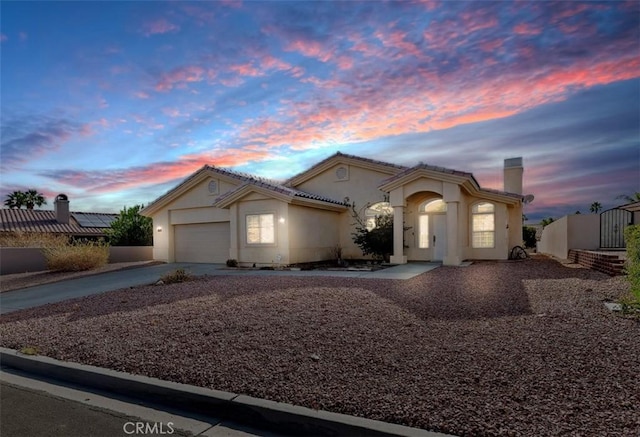 mediterranean / spanish-style home with a garage, fence, concrete driveway, stucco siding, and a chimney