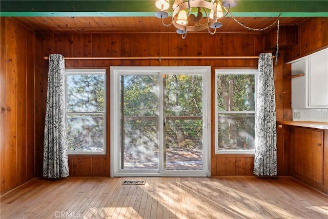 entryway featuring an inviting chandelier, wooden walls, wood ceiling, and light wood-type flooring