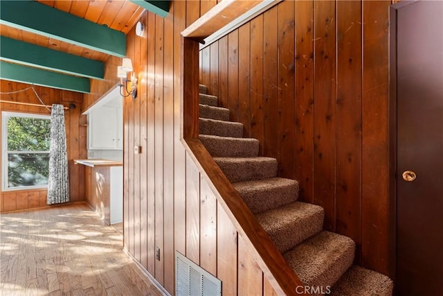 stairway with visible vents, beamed ceiling, wood finished floors, wood walls, and wood ceiling