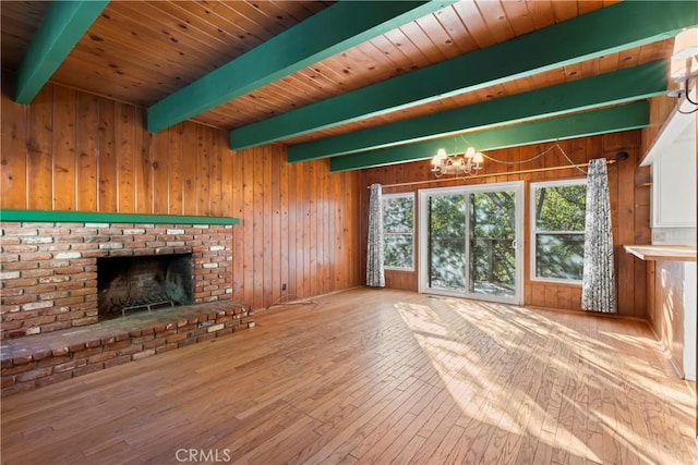 unfurnished living room featuring wooden walls, wood finished floors, beamed ceiling, a brick fireplace, and a chandelier