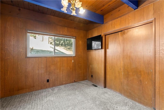 carpeted spare room featuring beam ceiling, a chandelier, wood ceiling, and wooden walls