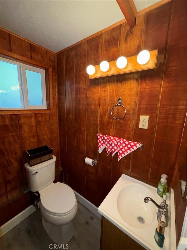 bathroom featuring beam ceiling, toilet, and wood walls