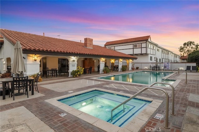 pool at dusk featuring a community hot tub and a patio