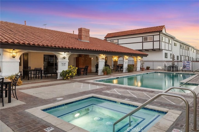 pool at dusk with a hot tub and a patio