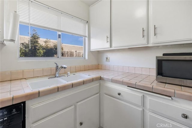 kitchen featuring tile counters, dishwasher, sink, and white cabinetry