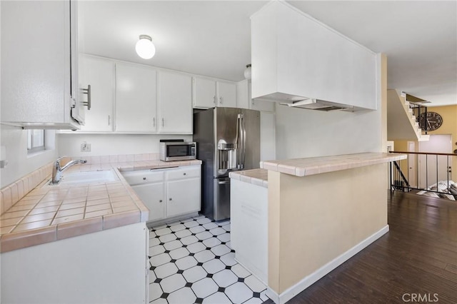 kitchen with kitchen peninsula, stainless steel appliances, tile counters, white cabinets, and sink