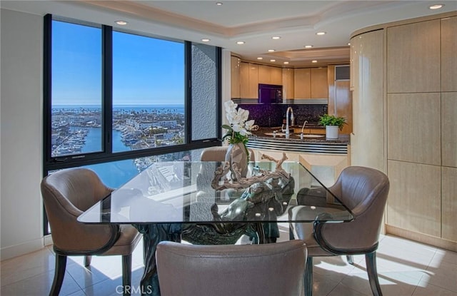 tiled dining room with sink, a tray ceiling, and a water view