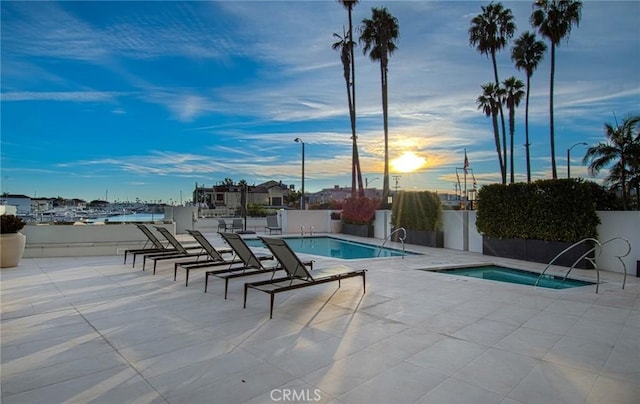 pool at dusk featuring a patio area and a community hot tub