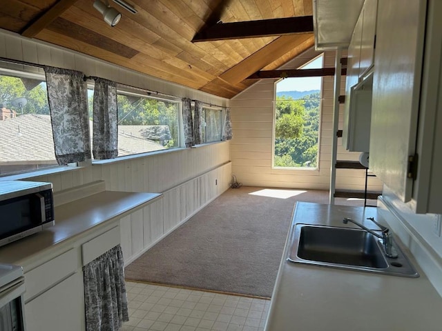 kitchen with lofted ceiling with beams, wooden walls, wood ceiling, light carpet, and white cabinets