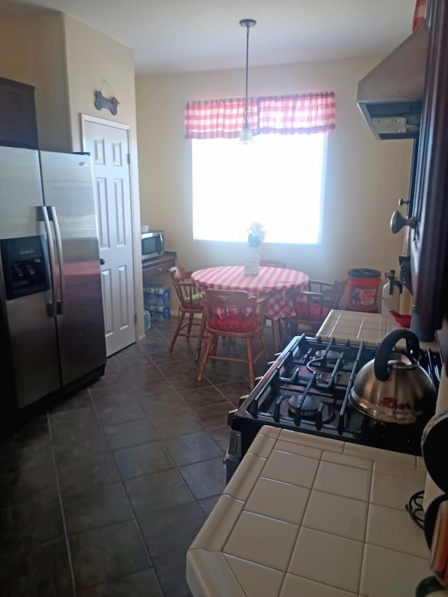 kitchen with stainless steel appliances, wall chimney range hood, and tile countertops