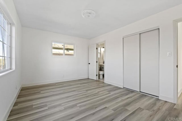 unfurnished bedroom with multiple windows, connected bathroom, light hardwood / wood-style floors, and a closet