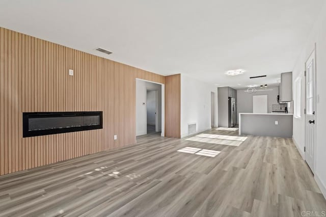 unfurnished living room with a notable chandelier, light hardwood / wood-style floors, a large fireplace, and wood walls