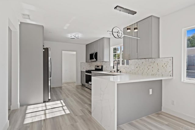 kitchen featuring sink, gray cabinets, kitchen peninsula, and appliances with stainless steel finishes